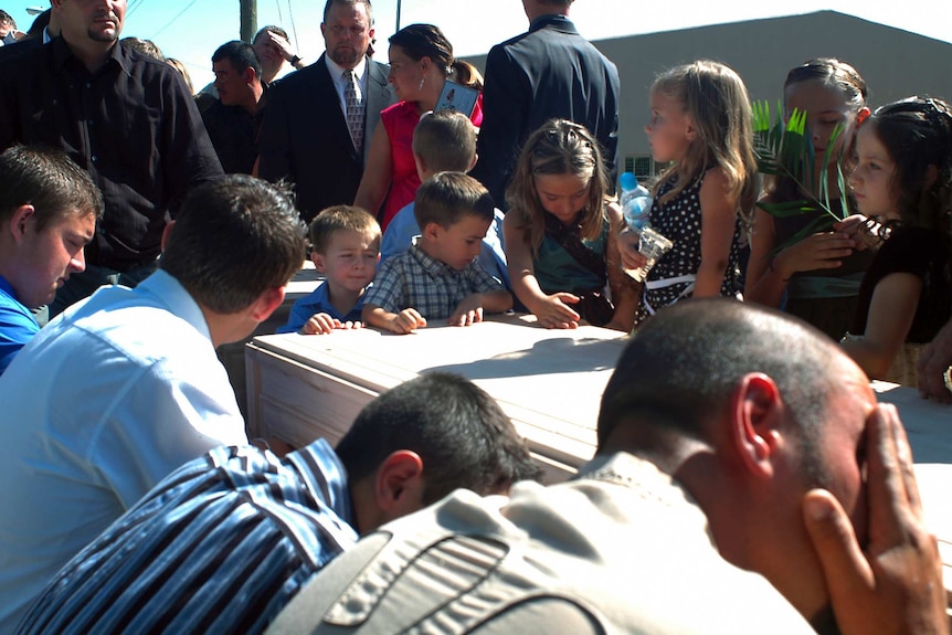 Kids with sombre faces surround a coffin at a funeral