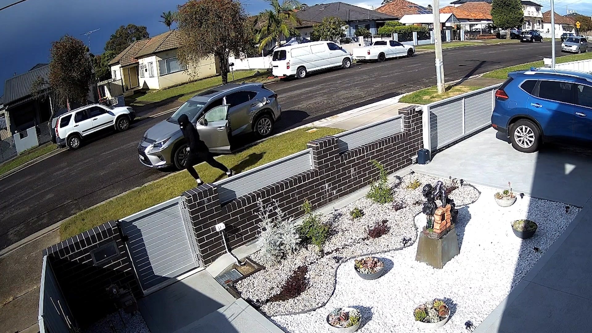 Man in all black runs from a grey car on a suburban street