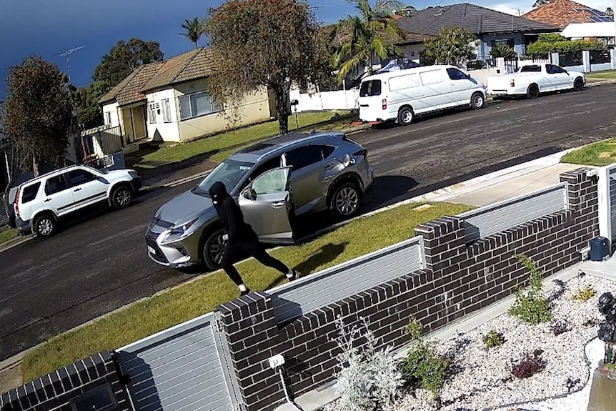 Man in all black runs from a grey car on a suburban street