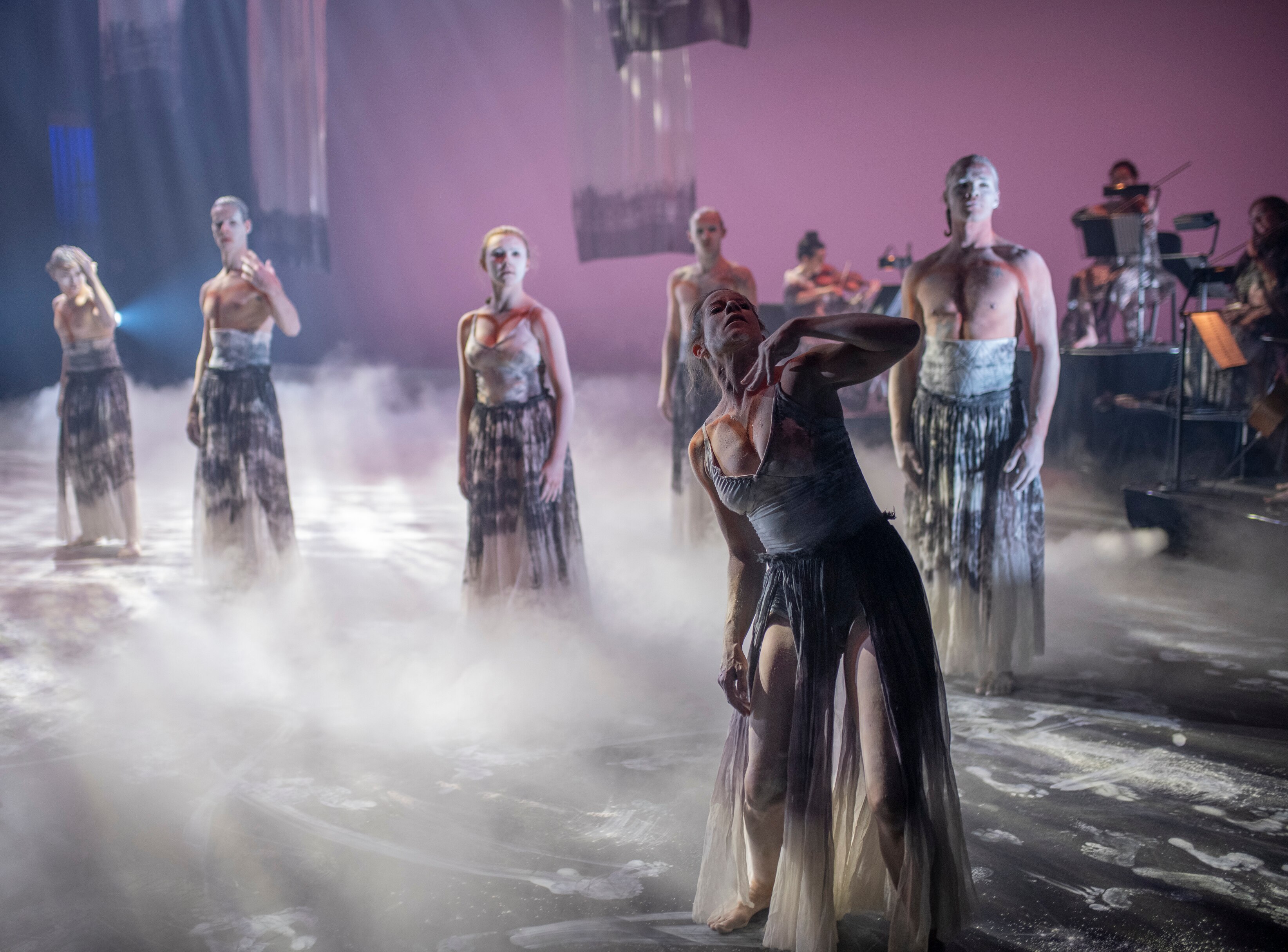 A group of dancers surrounded by smoke on stage.