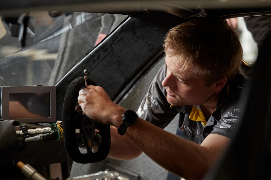 a young man reaches into a car fixing the steering wheel. 