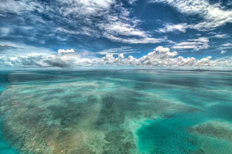 A reef in shallow tropical water with moody clouds overhead.