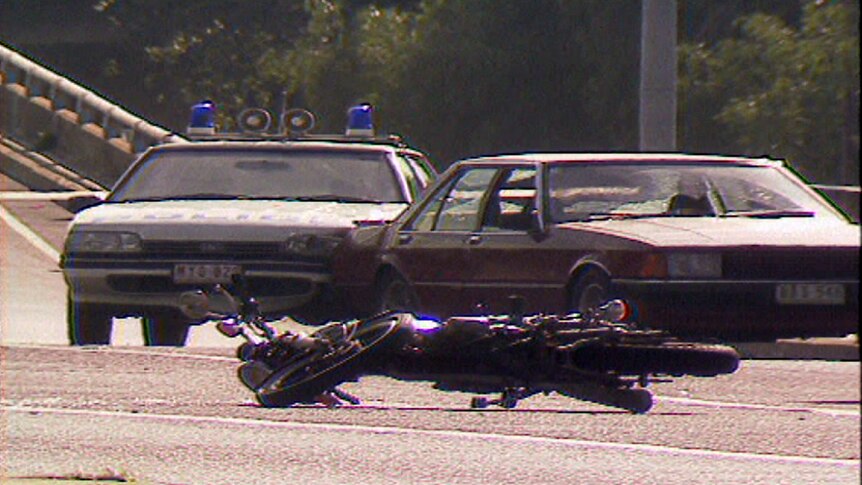 A motorbike lies on the road in front of a police care and another car after Hoddle St massacre.
