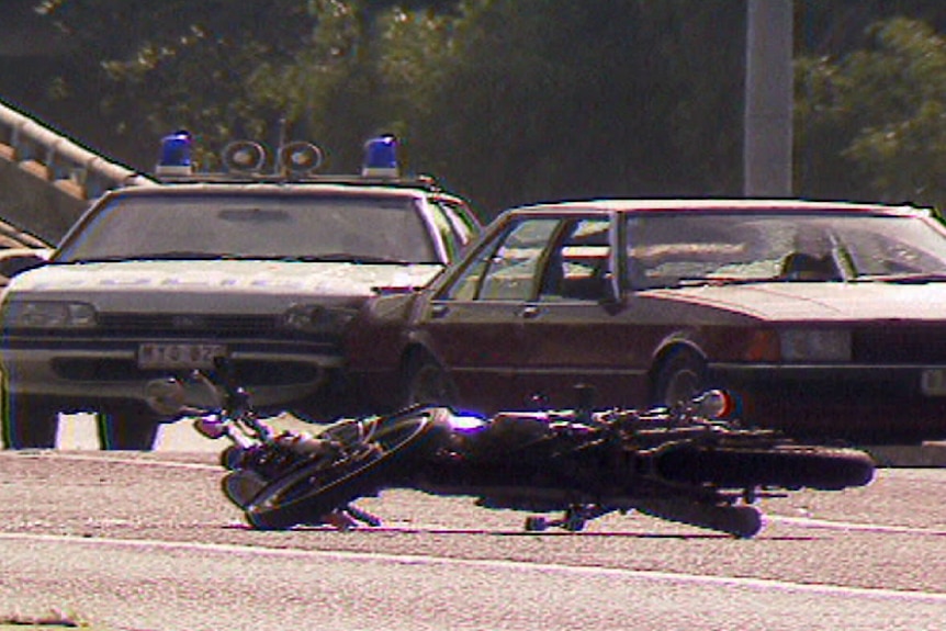 A motorbike lies on the road in front of a police care and another car after Hoddle St massacre.