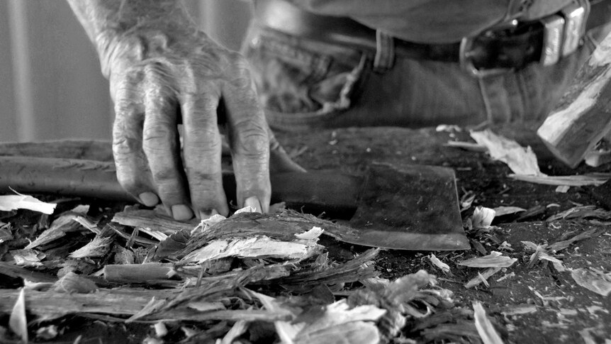 A black and white photo of Marshall Smith's hands holding an axe on a bench covered in wood shavings.