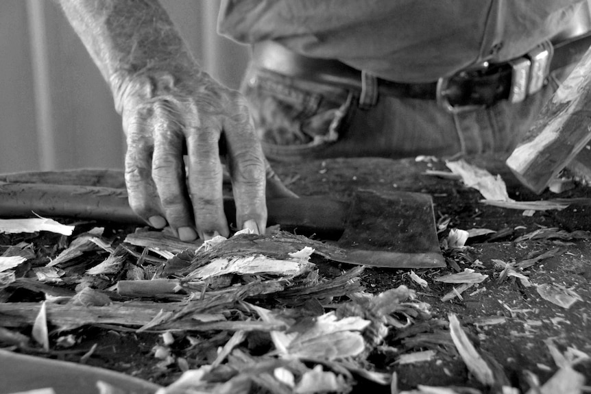 A black and white photo of Marshall Smith's hands holding an axe on a bench covered in wood shavings.