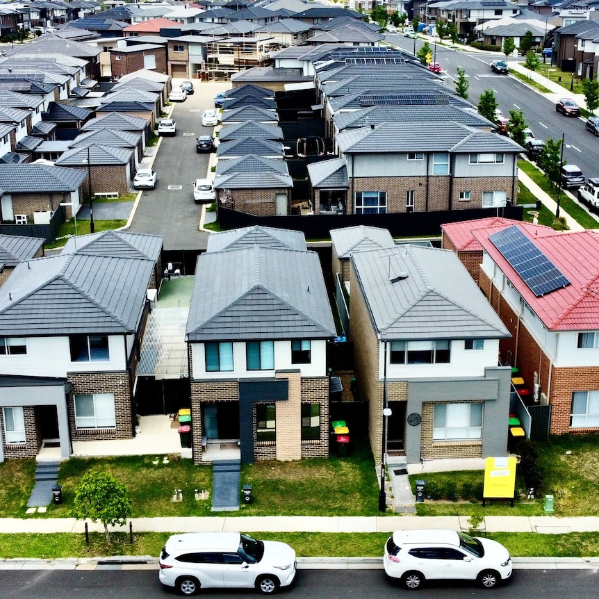 Aerial shot of dozens of houses in neat rows in a new outer-suburban housing estate.