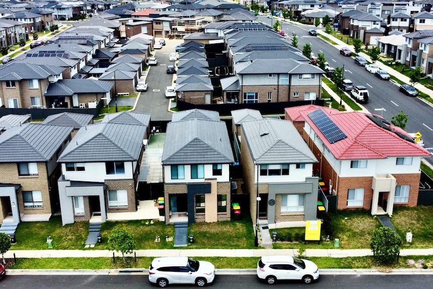 Toma aérea de docenas de casas en hileras ordenadas en una nueva urbanización suburbana.