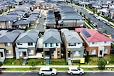 Aerial shot of dozens of houses in neat rows in a new outer-suburban housing estate.