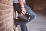 The lower half of a young man's body leans against a wall while holding a bible.