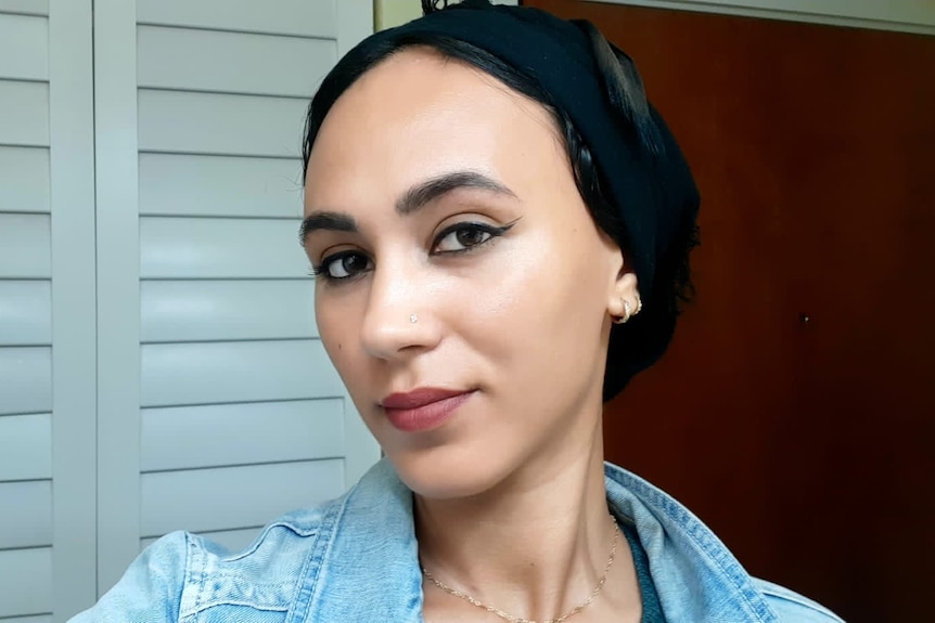 A young woman wearing a black headscarf and black eyeliner looks serious.