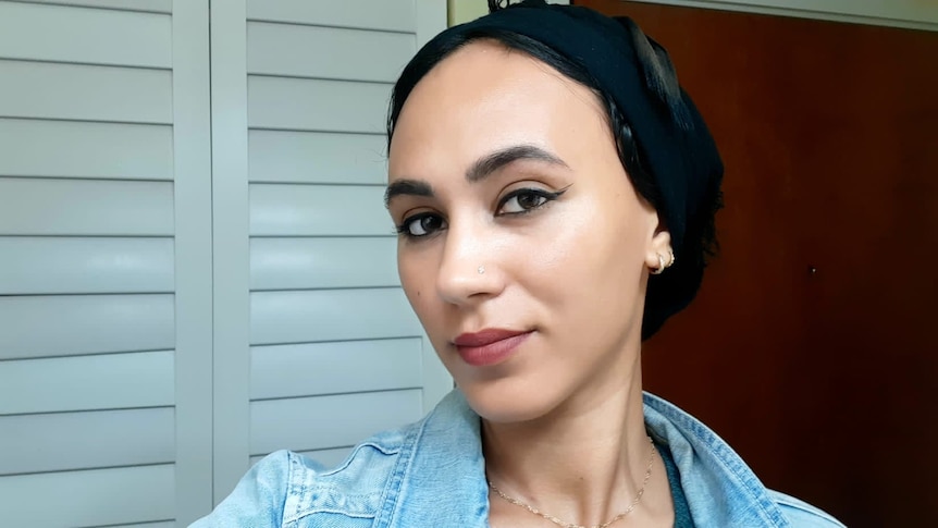 A young woman wearing a black headscarf and black eyeliner looks serious.