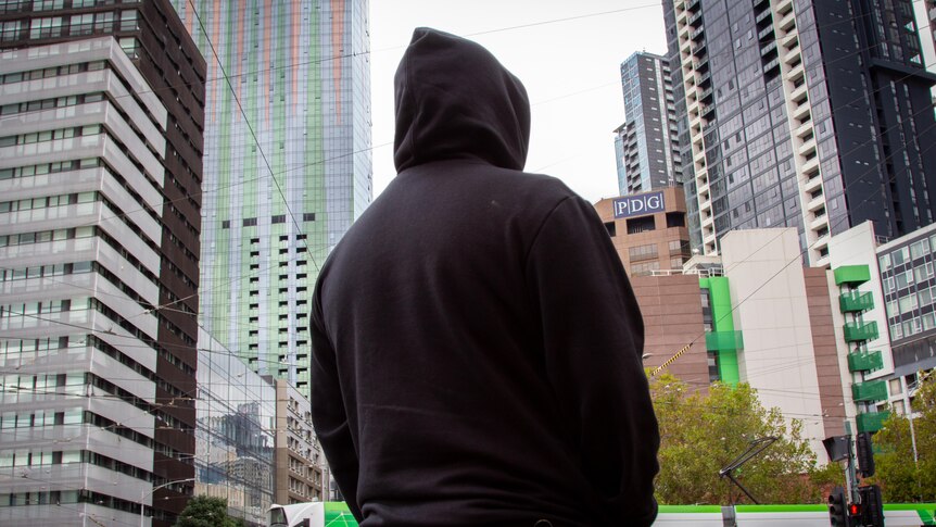 The back of a man in a black hoodie in front of buildings and a tram.