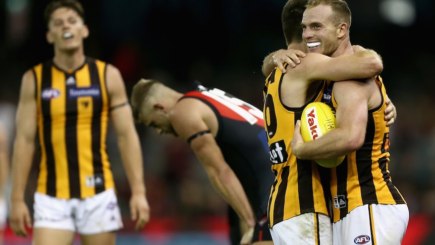 An AFL player holding the ball after the final siren is hugged by a teammate.