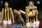 An AFL player holding the ball after the final siren is hugged by a teammate.