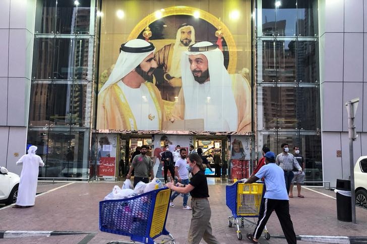 People are seen outside a shopping centre with a large portrait of two of Dubai's royal family in the main window.