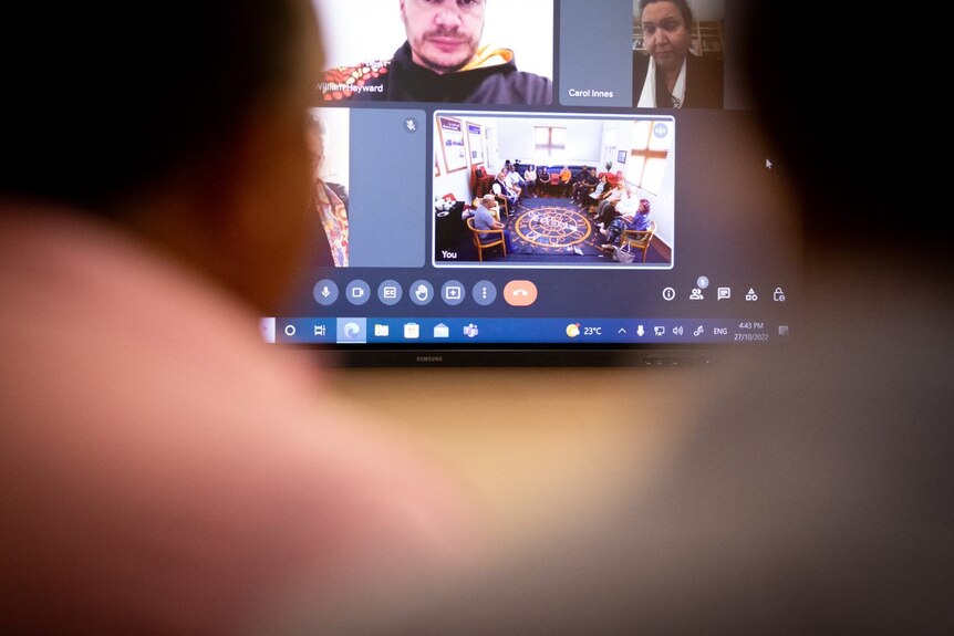 Two people in front of a computer screen with people's faces on it while they participate in a teleconference.