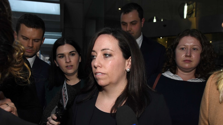 A woman with a radio microphone pointed at her in the centre of a group of men and women.