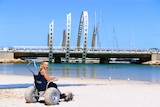 A young woman sits in a beach wheelchair on a beach.