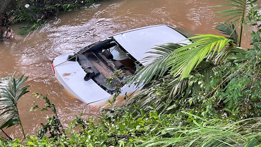 A white sedan in a narro creek surrounded by brown flodowaters.