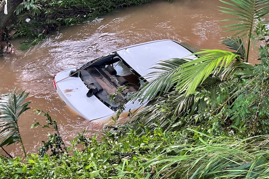 A white sedan in a narro creek surrounded by brown flodowaters.