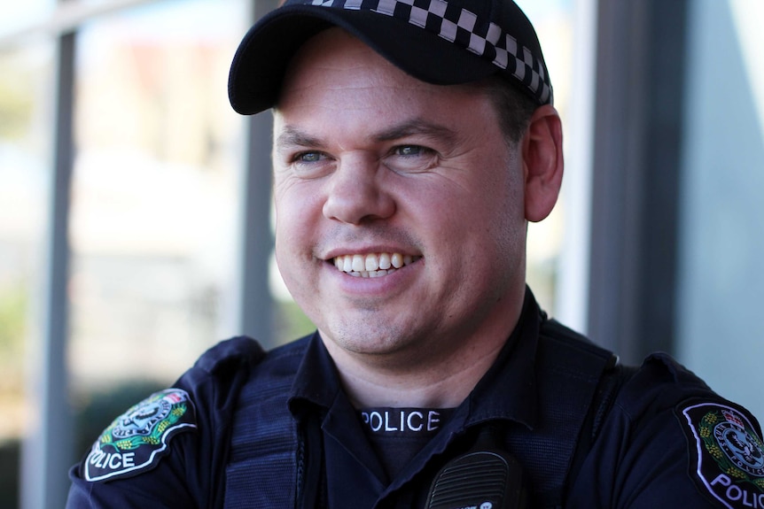 A close-up of a male police officer wearing a dark blue uniform and cap.
