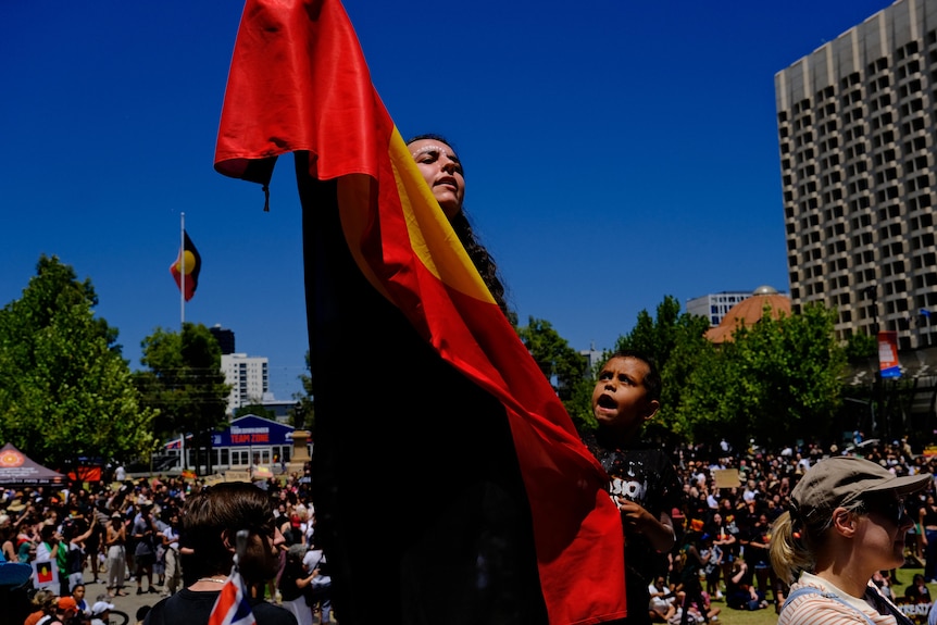 A young woman and a boy hold up an Aboriginal flag amid a protest and tall buildings