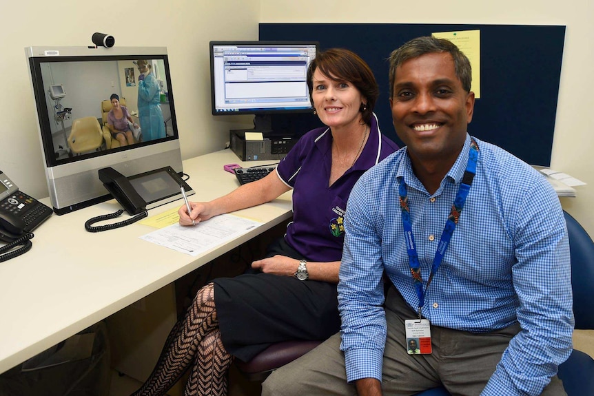 A doctor and nurse watch a patient on a video screen