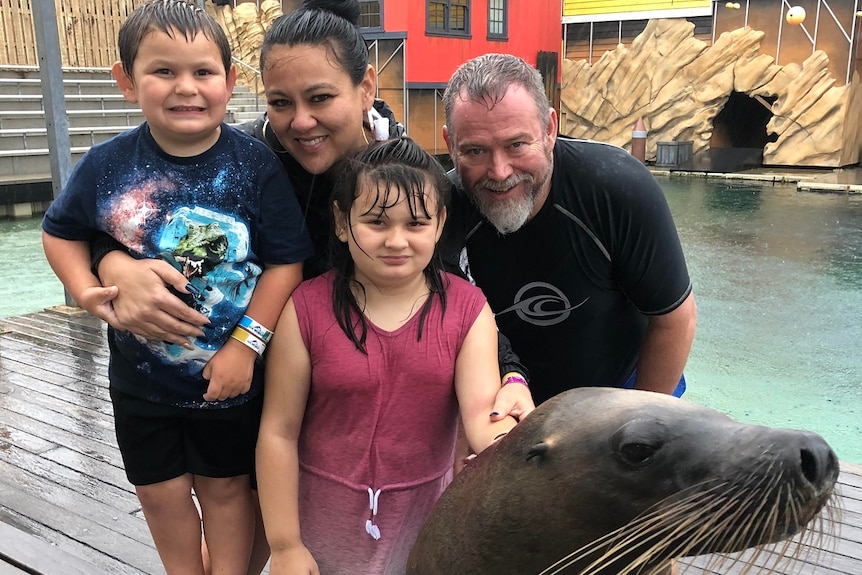 Carmen, Ashlee, Cooper and Adam smiling, sea lion in foreground, water behind.