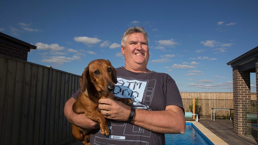 Craig Bolten standing in front of his pool with his dashund