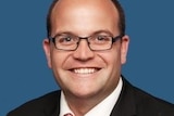 Man smiling wearing black framed glasses against blue background