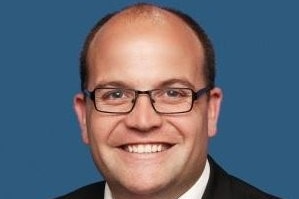 Man smiling wearing black framed glasses against blue background