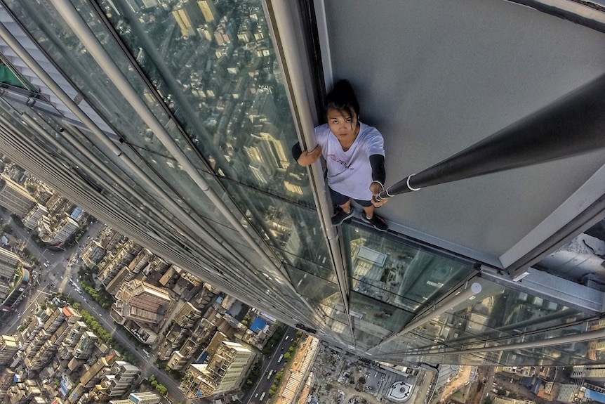 Wu Yongning takes a selfie while holding on to the window frame of a high-rise building.