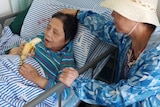 An elderly woman eats a banana in a hospital bed