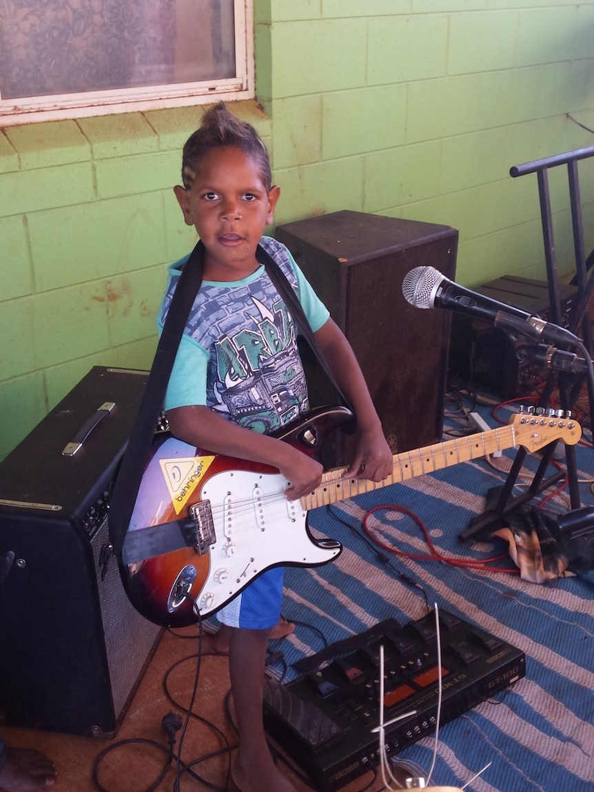 young boy with wearing a light blue t-shirt holding an electric guitar.