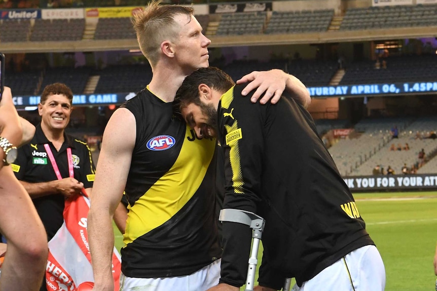 Jack Riewoldt puts an arm around Alex Rance, who leans on Riewoldt's shoulder as he stands with crutches and ice on his knee.