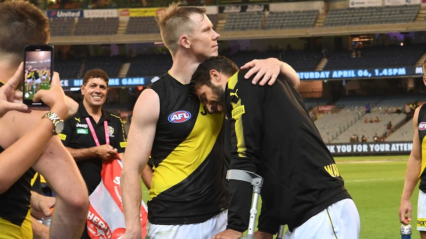 Jack Riewoldt puts an arm around Alex Rance, who leans on Riewoldt's shoulder as he stands with crutches and ice on his knee.
