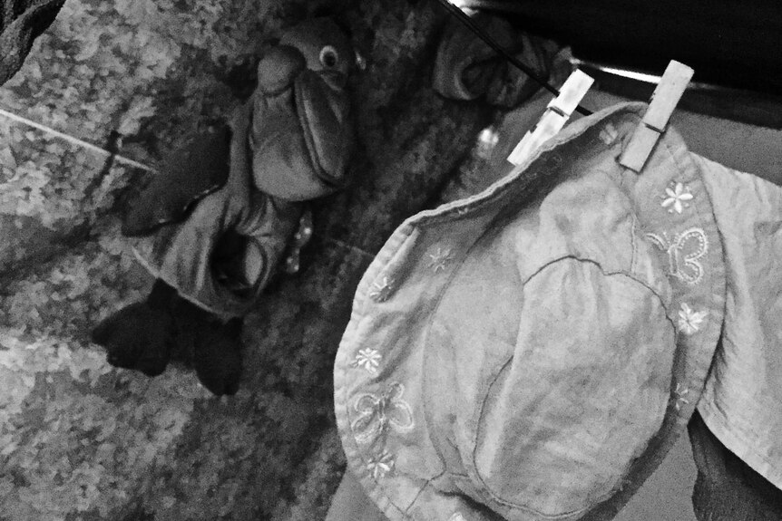 A child's hat and bag hang from a clothesline and the wall.