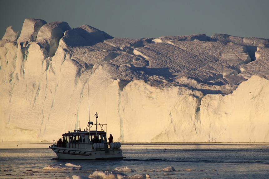 A boat passes an iceberg off the coast of Greenland during the Arctic summer in 2012
