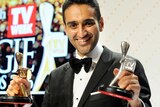 Waleed Aly holds his gold and silver Logies with a Logies sign behind him.