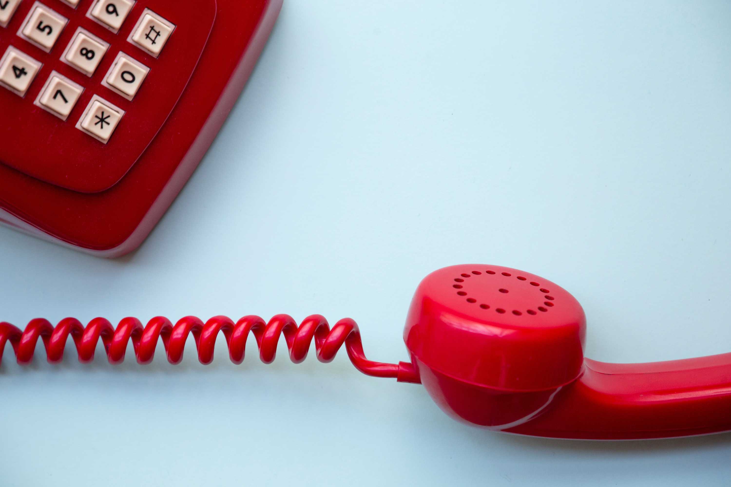 A red telephone on a blue background with is receiver lying in front of it.
