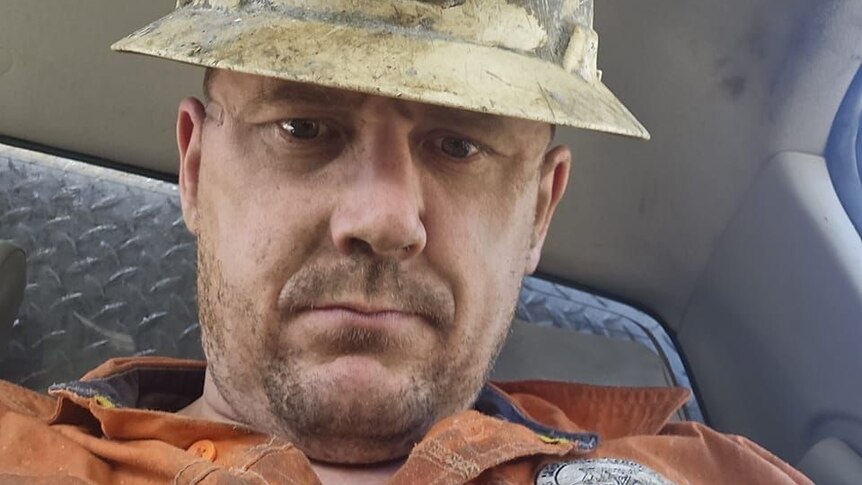 A serious-faced man in mining helmet looks at the camera.
