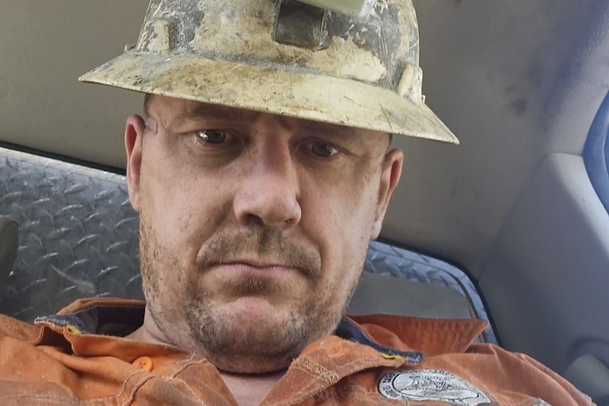 A serious-faced man in mining helmet looks at the camera.