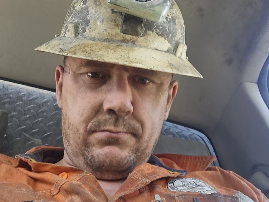 A serious-faced man in mining helmet looks at the camera.