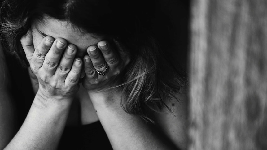 A black and white photo of a woman with her face in her hands.