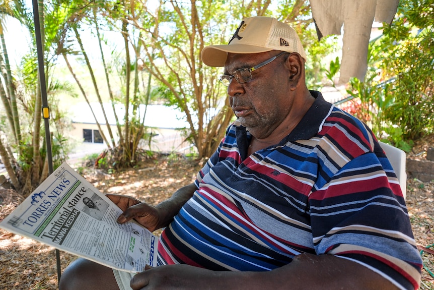 A man wearing a cap reads a newspaper