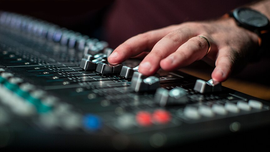 A hand with wedding ring and watch adjusting knobs on a sound desk