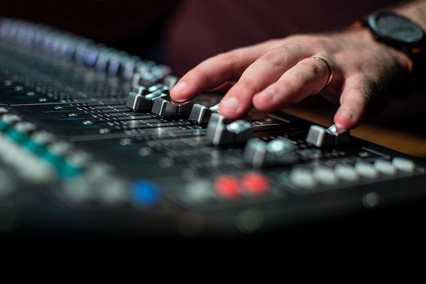 A hand with wedding ring and watch adjusting knobs on a sound desk