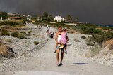 A man holds his daughter as he walks up a stone road followed by other tourists evacuating the island of Rhodes
