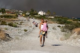 A man holds his daughter as he walks up a stone road followed by other tourists evacuating the island of Rhodes